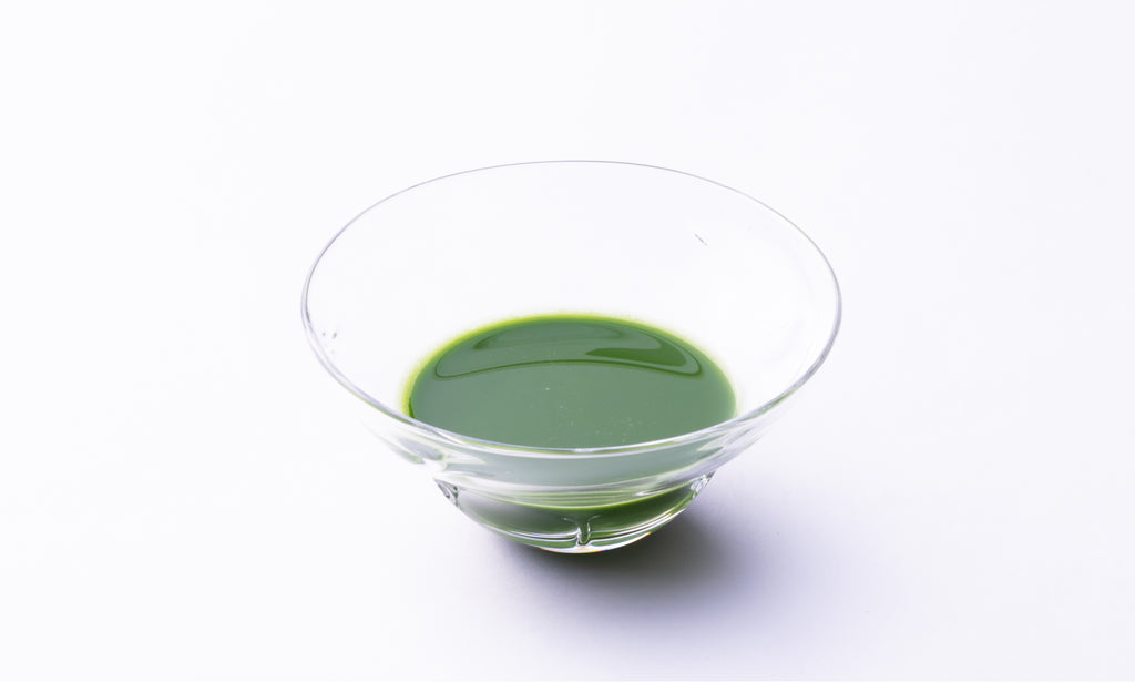 Thick dark green foamless Ippodo matcha tea in elegant prism-shaped decorative glass ware on white background