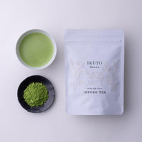 Teacup of green prepared matcha tea beside black plate of loose tea powder and white resealable bag of Ippodo Ikuyo matcha