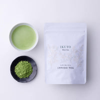 Teacup of green prepared matcha tea beside black plate of loose tea powder and white resealable bag of Ippodo Ikuyo matcha 