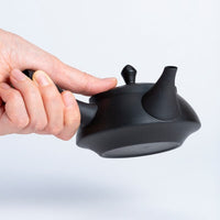 Hand holding black Ippodo Tea kyusu. Traditional Japanese teapot with left side handle, ready to pour.