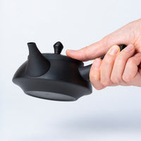 Hand holding black Ippodo Tea kyusu. Traditional Japanese teapot with side handle, ready to pour.