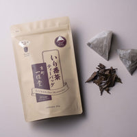 Tan and burgundy tea package with loose tea leaves and two pyramid-shaped tea bags on a light pink background