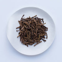 Sample of dried brown stems from Ippodo (Kuki) Stems Hojicha roasted bancha green tea stems on white plate, on white table