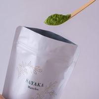Scooping spoonful of bright green matcha powder out of large white reseleable 40g bag of Sayaka by Ippodo Tea