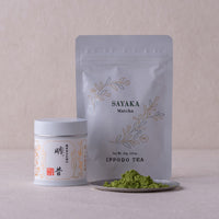 Lush green loose Sayaka matcha powder by Ippodo Tea on small silver plate beside tin and resealable bag packaging options
