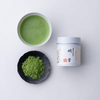 Teacup of bright green usucha matcha tea beside black plate of loose tea powder and white tin of Sayaka Matcha by Ippodo Tea