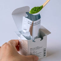 Box of Wakaki matcha with instructions on back and inner foil held open while scooping matcha powder with bamboo tea ladel