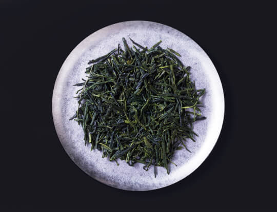 loose leaf dark green rolled dried Ippodo Tea Co. Gyokuro premium Japanese green tea on silver plate on black background