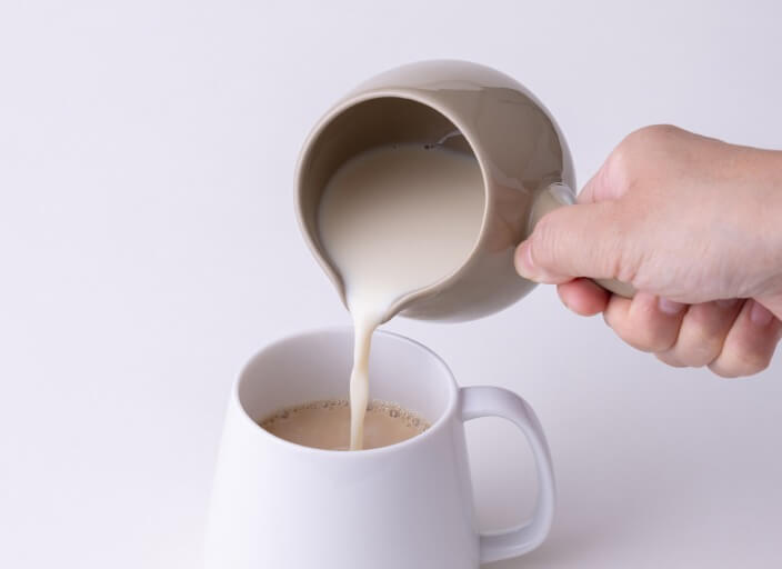 Pouring milk on top of amber Hojicha roasted green tea from white Hakuji ceramic (kyusu) teapot into white porcelain Japanese teacup