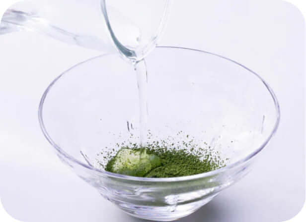 Pouring water from glass carafe into glass bowl of ultra fine powder sifted Ippodo Tea Co. matcha green tea powder