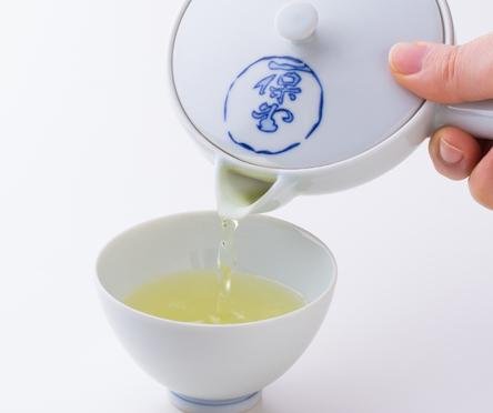 Pouring light green tea from white porcelain Hasami-yaki kyusu teapot with blue logo into white porcelain Japanese teacup