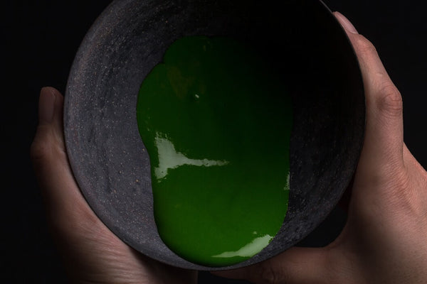 Vivid green smooth thick koicha Ippodo Premium Select Matcha sticking to sides of tilted black artisan-made ceramic tea bowl 