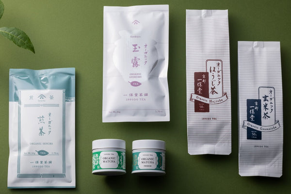 Assortment of white packages and tins of organic Ippodo Teas and matchas with tasteful designs beside a green leaf on a green table 