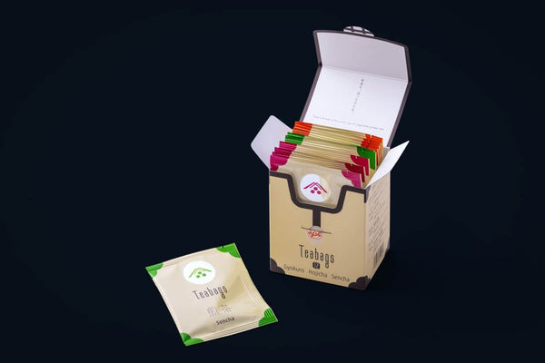Assortment of white packages and tins of organic Ippodo Teas and matchas with tasteful designs beside a green leaf on a green table