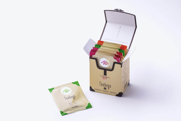 Assortment of white packages and tins of organic Ippodo Teas and matchas with tasteful designs beside a green leaf on a green table