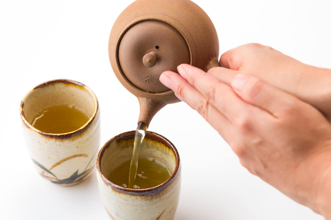 Serving green tea from brown clay Ippodo Yakishime Kyusu Japanese Banko-yaki teapot into two tall brown handmade ceramic cups