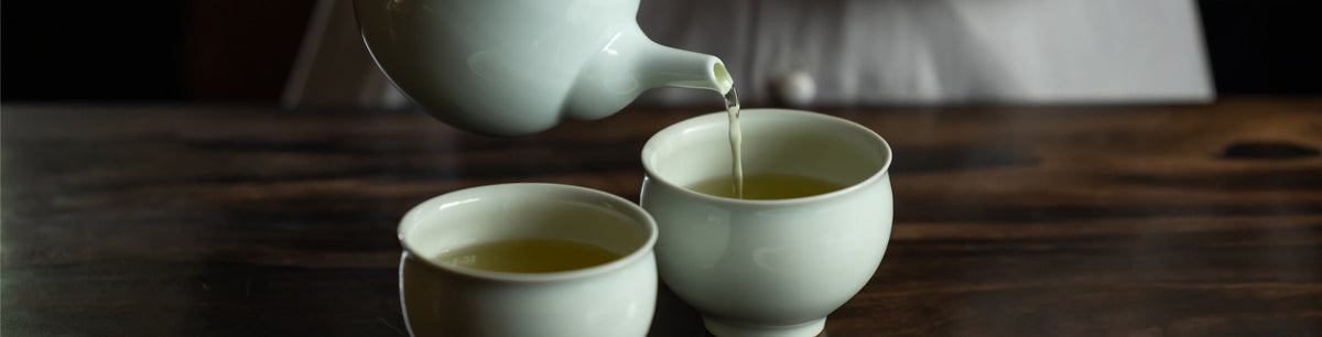 Tea being poured from a porcelain teapot until porcelain cups