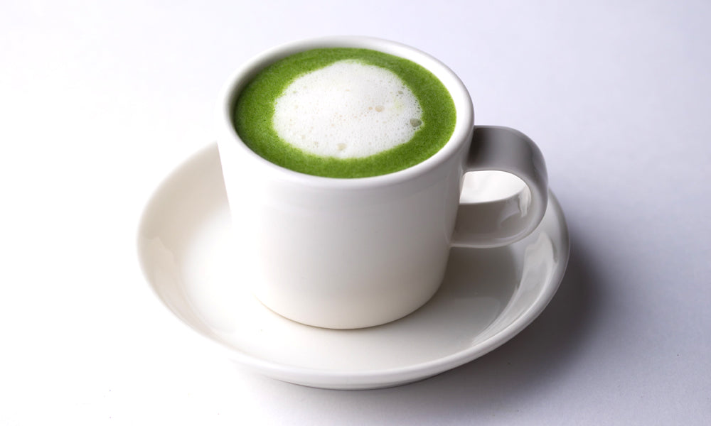 Vivid green matcha latte with dollop of foamed milk on top of pure matcha tea base in white espresso cup with matching saucer