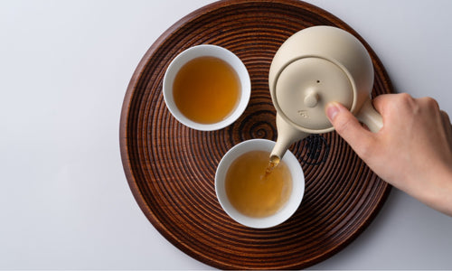 Pouring roasted Hojicha tea from Ivory Kyusu into white Hasami-yaki porcelain teacups on wood cross-section Marubon tray