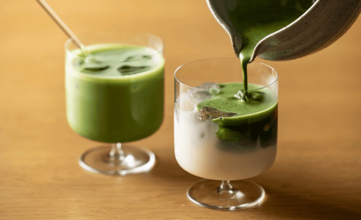 Pouring vibrant green matcha float from spouted bowl over milk and ice in elegant stemmed glassware beside iced matcha latte