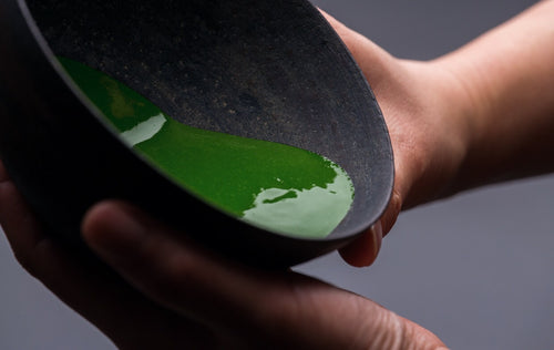 Verdant green smooth and thick koicha Ippodo matcha in tilted black artisan-crafted ceramic tea bowl and coating the sides