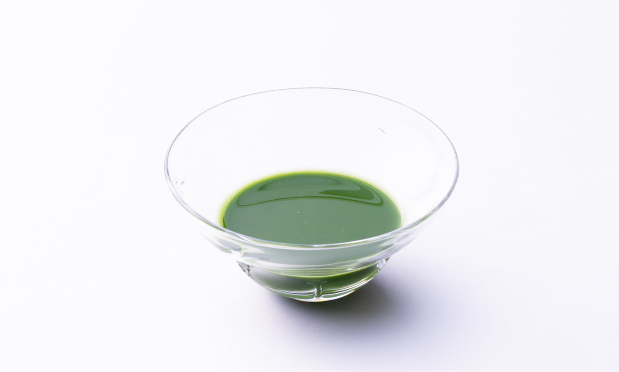 Thick dark green foamless Ippodo matcha tea in elegant prism-shaped decorative glass ware on white background