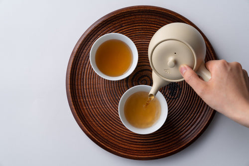 Pouring roasted Hojicha tea from Ivory Kyusu into white Hasami-yaki porcelain teacups on wood cross-section Marubon tray