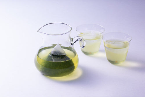 Teapot-sized Shincha Teabag steeping in a glass pitcher of cold brewed light green tea beside two glasses of sencha tea.