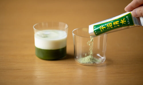 To go travel stick of Ippodo Uji-Shimizu sweetened green matcha powder sprinkled into modern glass beside extra foamy matcha