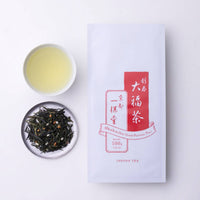 Porcelain teacup of Obukucha green tea beside plate of loose Good Fortune tea with roasted rice and red Ippodo Tea packaging 