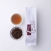 Porcelain teacup of amber roasted green tea beside plate of roasted leaves stems and package of Ippodo Tea Organic Hojicha