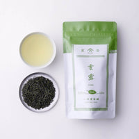 Teacup of misty golden brewed sencha green tea with silver plate of loose tea leaves and green packaging for Unro Ippodo Tea