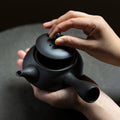 Hands opening a black Ippodo Tea kyusu. Round Japanese teapot with side handle and lid. Green tea preparation.