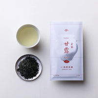 Teacup of brewed straw-colored gyokuro green tea alongside plate of dark green tea leaves and packaging for Ippodo Tea Kanro