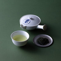 Small white porcelain Ippodo teapot and teacup of light color Japanese gyokuro tea beside silver plate of loose green tea