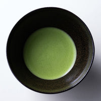 Green thin usucha straight Ippodo matcha with light green frothy bubbles on surface in black colored ceramic tea bowl