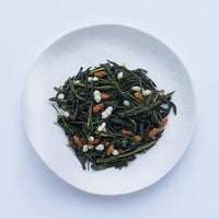 Sample of Ippodo Genmaicha dried bancha green tea leaves and stems mixed with roasted rice on white plate, on white table