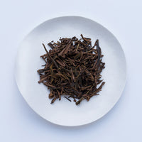 Sample of Ippodo Hojicha roasted green tea leaves and stems on white plate, on white table