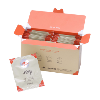 Open box filled with Ippodo hojicha tea bag packets with orange accents, alongside a single hojicha packet in front.