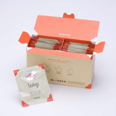Open box filled with Ippodo hojicha tea bag packets with orange accents, alongside a single hojicha packet in front.
