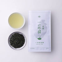 Teacup of straw-colored Japanese green tea beside silver plate of loose leaf tea and white bag of Ippodo Ippoen gyokuro 