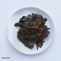 Deep brown roasted bancha green tea leaves and stems from Kyoto on white plate on white table