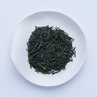 White plate of dark green dried premium loose leaf Japanese Kaboku Sencha tea leaves by Ippodo Tea Co. on white table