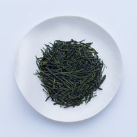 White plate of dark green dried premium loose leaf Japanese Kumpu Sencha tea leaves by Ippodo Tea Co. on white table