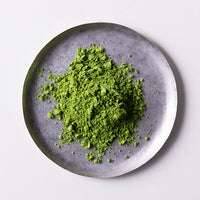 Loose green finely ground premium verdant green Japanese Ippodo Kuon Matcha tea powder on silver plate on white table