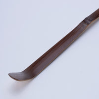 Mahogany brown curved matcha tea ladle utensil on a light gray background