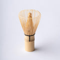 100-tip bamboo chasen matcha whisk tea utensil with curles tips resting upright on handle on white table