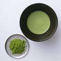 Dark tea bowl of prepared new harvest matcha usucha thin tea beside silver plate with loose green powder