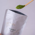 Scooping spoonful of bright green matcha powder out of large white reseleable 40g bag of Sayaka by Ippodo Tea