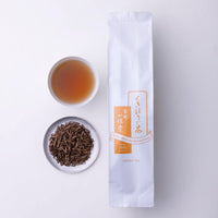 Porcelain teacup of amber roasted green tea and plate of roasted stems with orange and white package of Ippodo Stems Hojicha